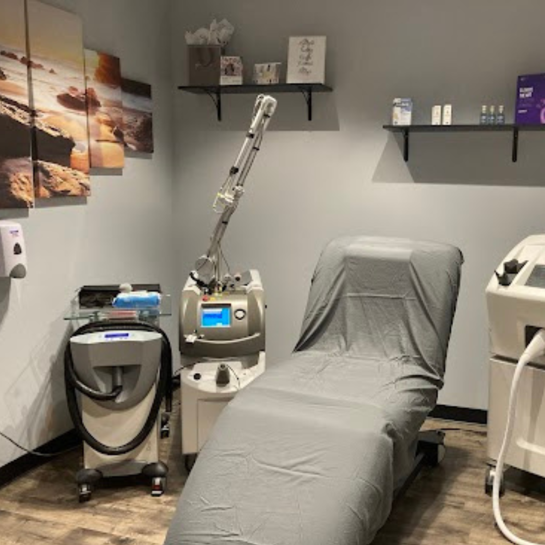 Laser tattoo removal treatment room at Cascade Medical Spa in Portland, featuring a Q-Plus C Evo laser, a cooling system, treatment chair, and neatly organized skincare shelves.